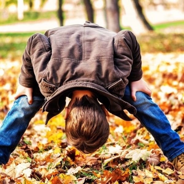 Menino brincando no jardim olhando por baixo de suas próprias pernas depois de se curar de Artrite crônica da infância