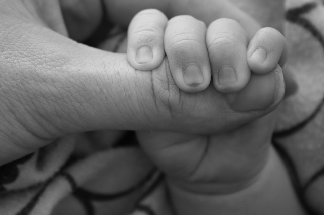 Mão de bebê pega com segurança no dedão do pai que o traz com carinho nos braços mostrando vínculo afetivo entre pai e filho